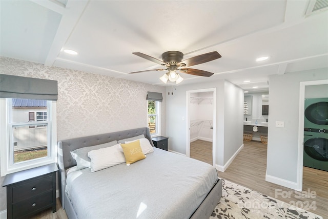 bedroom with a closet, light hardwood / wood-style flooring, a spacious closet, stacked washer / dryer, and ceiling fan