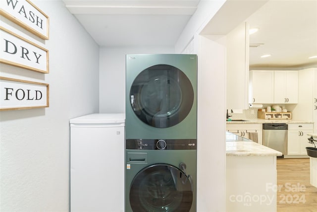 clothes washing area featuring sink, light hardwood / wood-style flooring, and stacked washer and clothes dryer