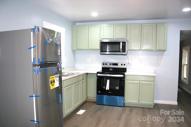 kitchen with wood-type flooring, appliances with stainless steel finishes, green cabinets, and sink