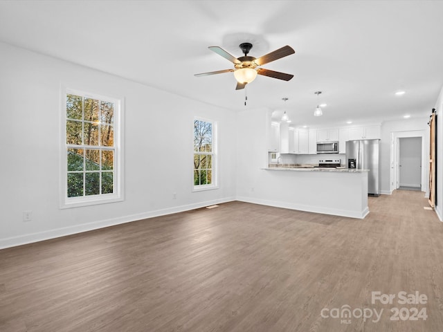 unfurnished living room featuring plenty of natural light, a barn door, light wood-type flooring, and ceiling fan