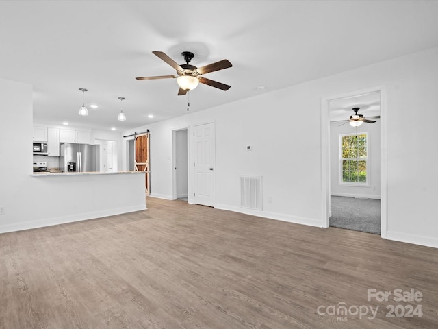 unfurnished living room featuring a barn door, ceiling fan, and hardwood / wood-style floors