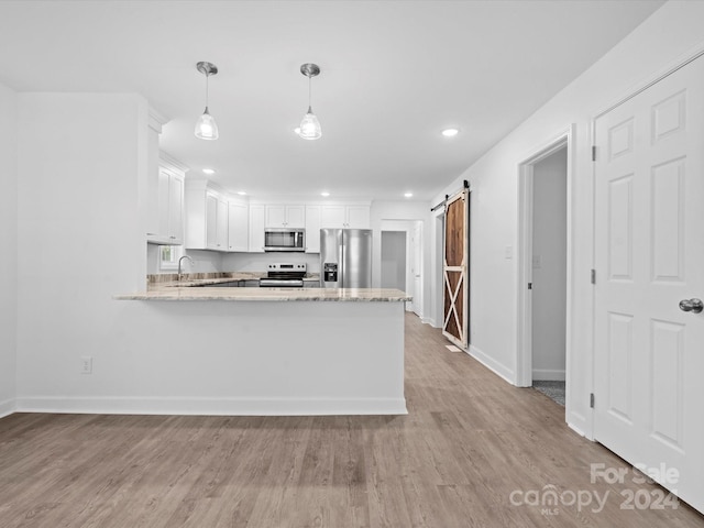 kitchen with appliances with stainless steel finishes, a barn door, decorative light fixtures, light hardwood / wood-style flooring, and white cabinetry