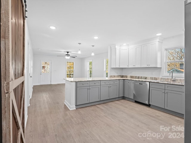 kitchen featuring kitchen peninsula, stainless steel dishwasher, sink, a barn door, and white cabinetry