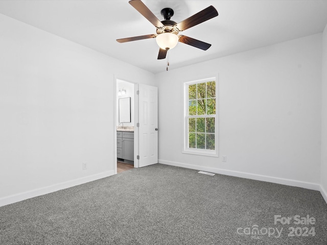 unfurnished bedroom with dark colored carpet, ensuite bath, ceiling fan, and sink