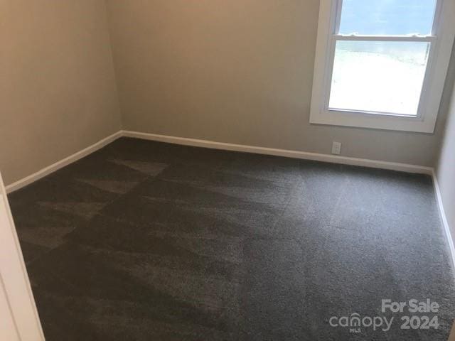 unfurnished room featuring dark colored carpet and baseboards