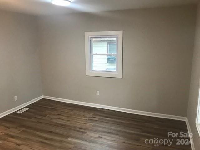 spare room featuring baseboards, dark wood-style flooring, and visible vents