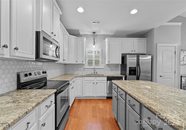 kitchen with white cabinets, sink, light hardwood / wood-style flooring, decorative light fixtures, and stainless steel appliances