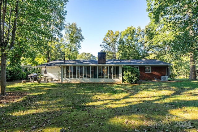 rear view of house featuring central air condition unit, a sunroom, and a lawn