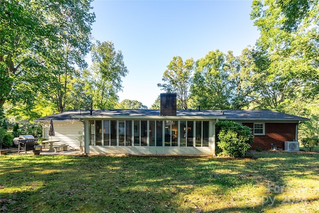 rear view of property with central AC unit, a sunroom, and a lawn