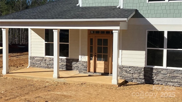 view of exterior entry with stone siding and roof with shingles