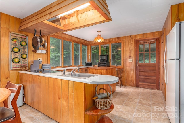 kitchen featuring white refrigerator, kitchen peninsula, wooden walls, sink, and light tile patterned floors