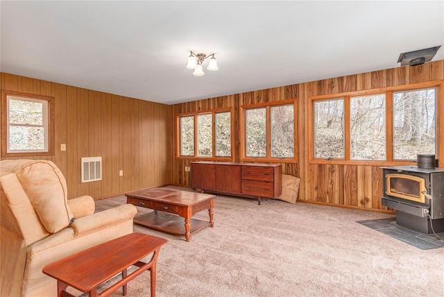 carpeted living room with a wood stove, a wealth of natural light, and wooden walls