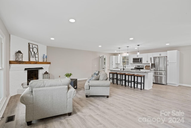 living room featuring light hardwood / wood-style flooring, sink, and a brick fireplace