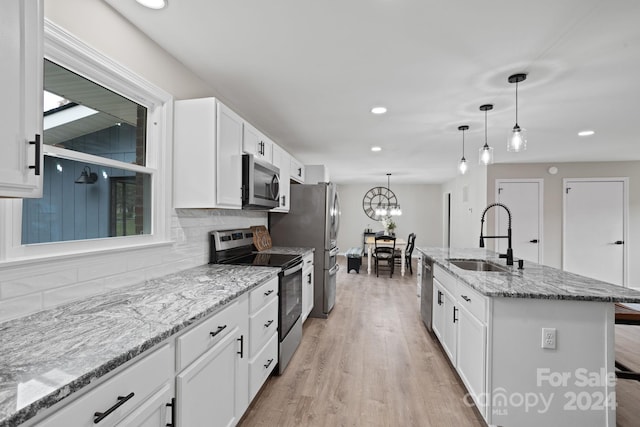 kitchen featuring appliances with stainless steel finishes, white cabinets, sink, and an island with sink