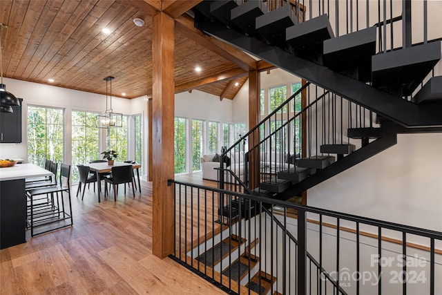 staircase with high vaulted ceiling, wood ceiling, hardwood / wood-style floors, beam ceiling, and a notable chandelier