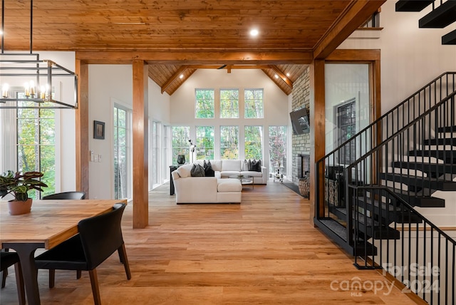 living room featuring wood ceiling, beam ceiling, an inviting chandelier, a stone fireplace, and light hardwood / wood-style floors