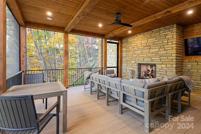 sunroom with beamed ceiling, an outdoor stone fireplace, ceiling fan, and wooden ceiling