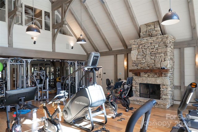 exercise room with a stone fireplace, hardwood / wood-style flooring, high vaulted ceiling, and wooden walls