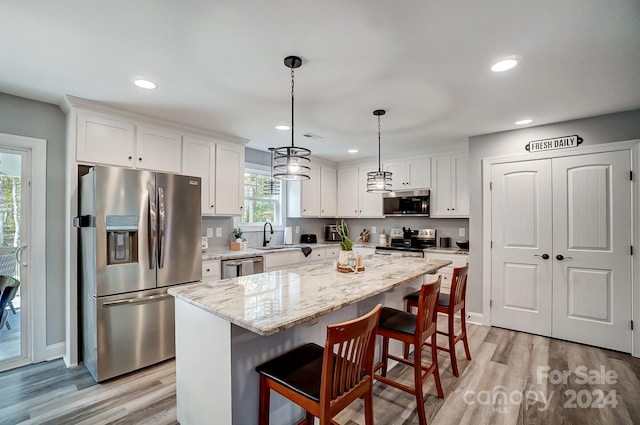 kitchen with white cabinets, appliances with stainless steel finishes, a center island, and decorative light fixtures