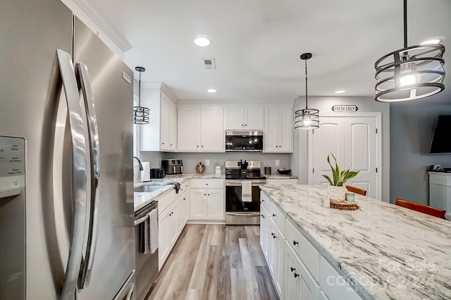 kitchen featuring appliances with stainless steel finishes, light stone countertops, hanging light fixtures, white cabinets, and light hardwood / wood-style flooring