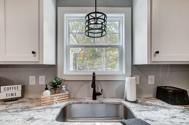 room details with white cabinets, sink, pendant lighting, and light stone counters