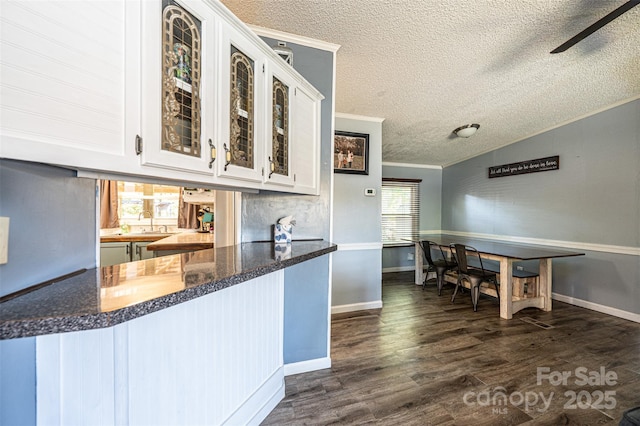 kitchen with white cabinetry, kitchen peninsula, dark hardwood / wood-style flooring, vaulted ceiling, and crown molding