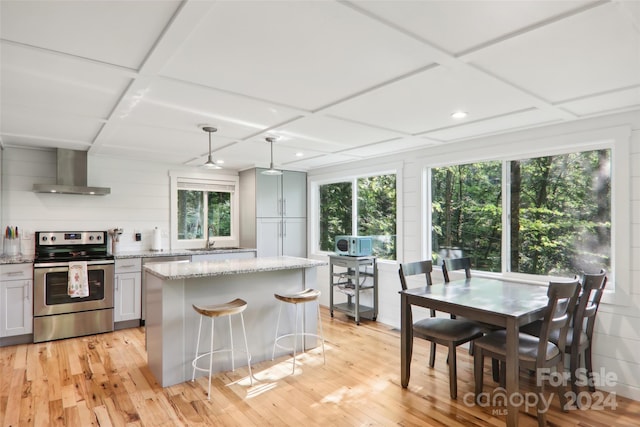 kitchen with stainless steel range with electric stovetop, a healthy amount of sunlight, wall chimney range hood, and pendant lighting