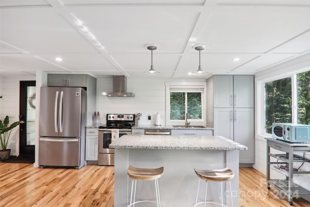 kitchen featuring stainless steel appliances, wall chimney range hood, a wealth of natural light, and hanging light fixtures