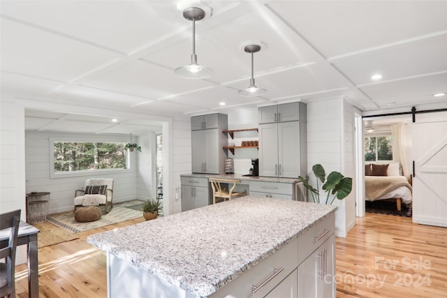 kitchen with hanging light fixtures, a kitchen island, a barn door, light hardwood / wood-style floors, and light stone counters