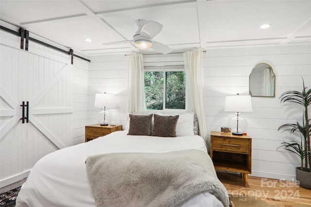 bedroom with ceiling fan, hardwood / wood-style flooring, a barn door, and wood walls