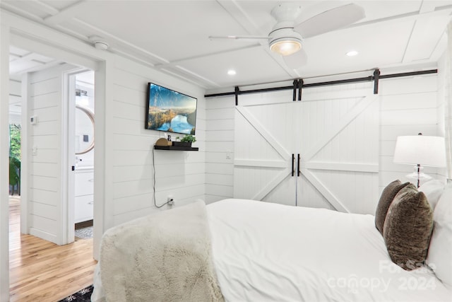 bedroom with wood-type flooring, ensuite bath, a barn door, ceiling fan, and wood walls