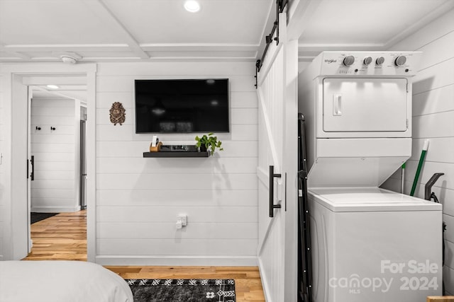 clothes washing area with hardwood / wood-style flooring, stacked washer and dryer, a barn door, and wood walls