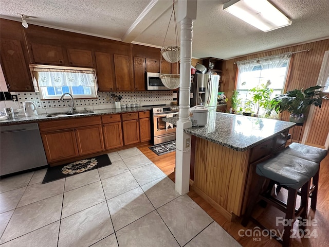 kitchen with dark stone countertops, stainless steel appliances, a textured ceiling, and a breakfast bar area