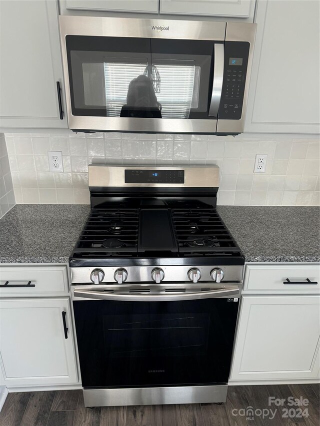 kitchen featuring appliances with stainless steel finishes, white cabinetry, stone counters, and dark hardwood / wood-style flooring