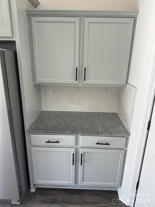 kitchen featuring dark wood-type flooring, light stone counters, tasteful backsplash, and stainless steel refrigerator