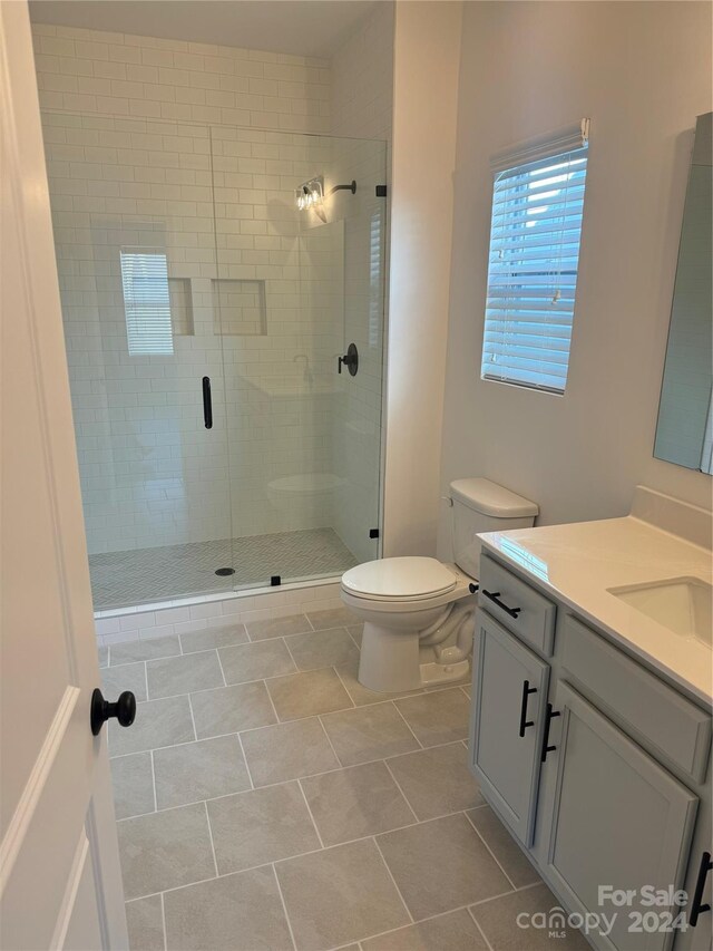 bathroom with a shower with door, vanity, toilet, and tile patterned flooring