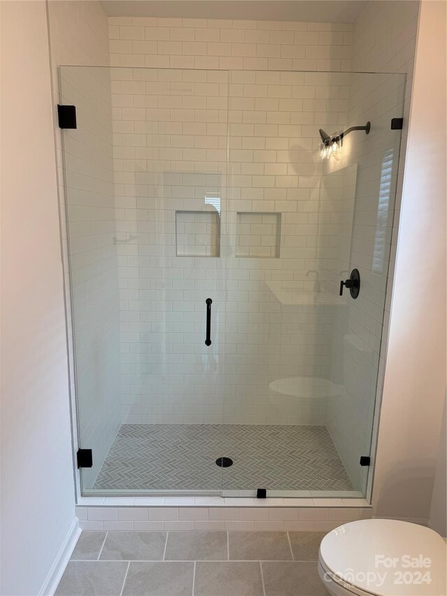 bathroom featuring tile patterned floors, a shower with shower door, and toilet