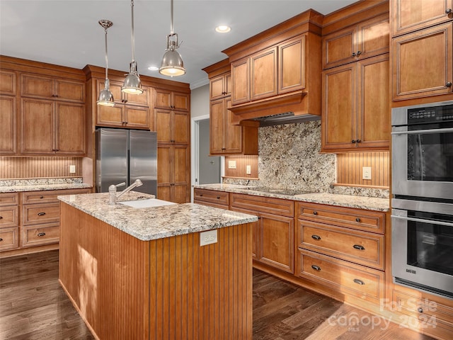 kitchen with appliances with stainless steel finishes, decorative light fixtures, dark hardwood / wood-style floors, and a kitchen island with sink