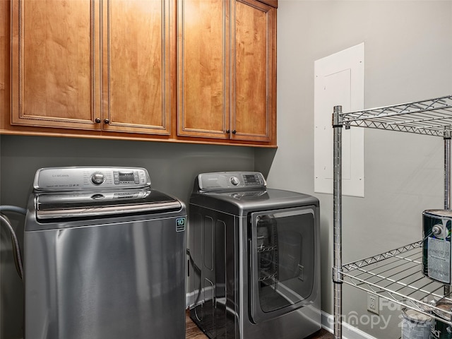 clothes washing area featuring electric panel, washing machine and clothes dryer, and cabinets