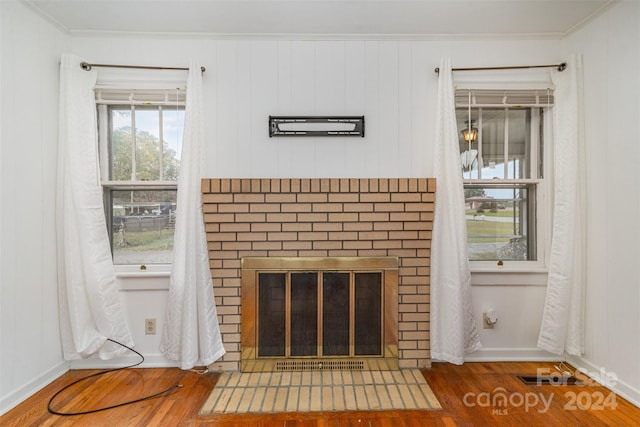 unfurnished living room with hardwood / wood-style floors, crown molding, and a brick fireplace