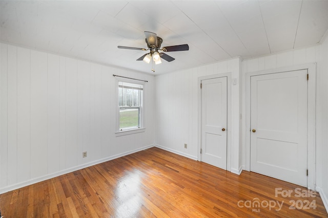 spare room with hardwood / wood-style floors, ceiling fan, and wood walls