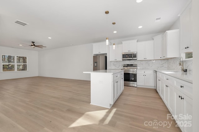 kitchen featuring white cabinets, a kitchen island, decorative light fixtures, stainless steel appliances, and sink