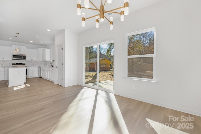 unfurnished dining area featuring an inviting chandelier and light hardwood / wood-style flooring