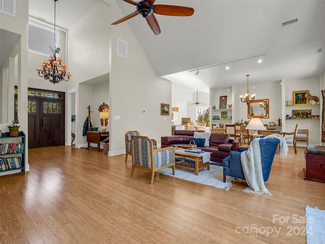 living room with a healthy amount of sunlight, light hardwood / wood-style floors, high vaulted ceiling, and ceiling fan with notable chandelier