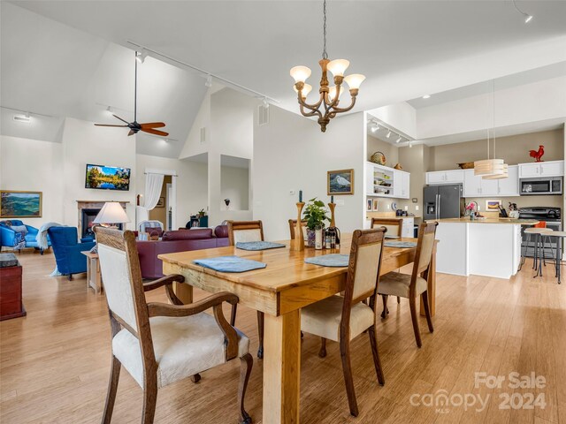 dining room featuring track lighting, high vaulted ceiling, light wood-type flooring, and ceiling fan with notable chandelier