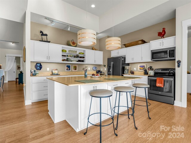 kitchen with appliances with stainless steel finishes, decorative light fixtures, white cabinetry, and an island with sink