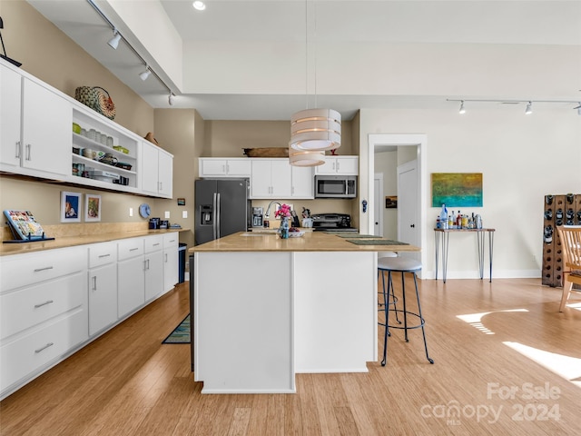 kitchen with an island with sink, electric range, white cabinetry, a breakfast bar area, and refrigerator with ice dispenser