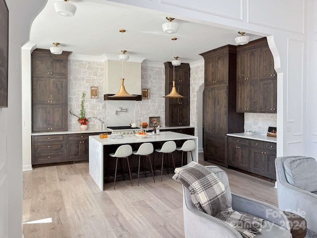 kitchen with decorative backsplash, a kitchen island with sink, a kitchen bar, pendant lighting, and light wood-type flooring