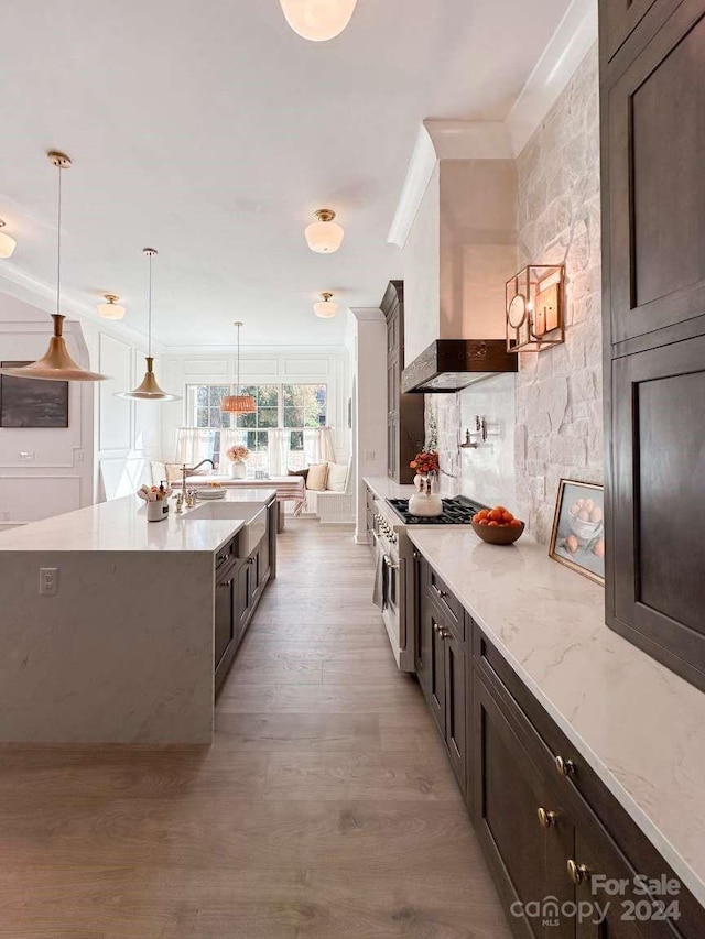 kitchen with wall chimney range hood, stainless steel gas cooktop, pendant lighting, light stone counters, and light hardwood / wood-style flooring