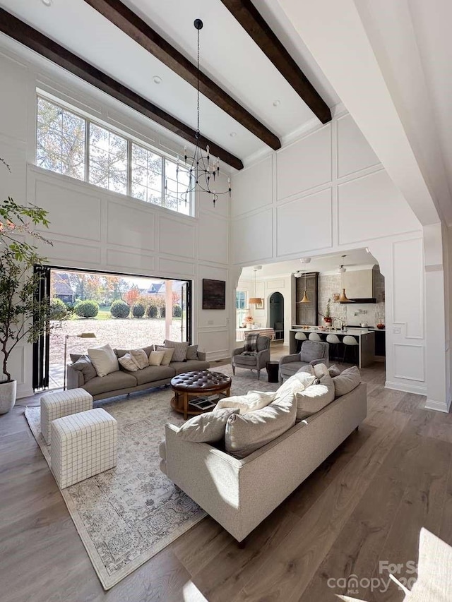 living room featuring beam ceiling, a towering ceiling, a chandelier, and hardwood / wood-style floors